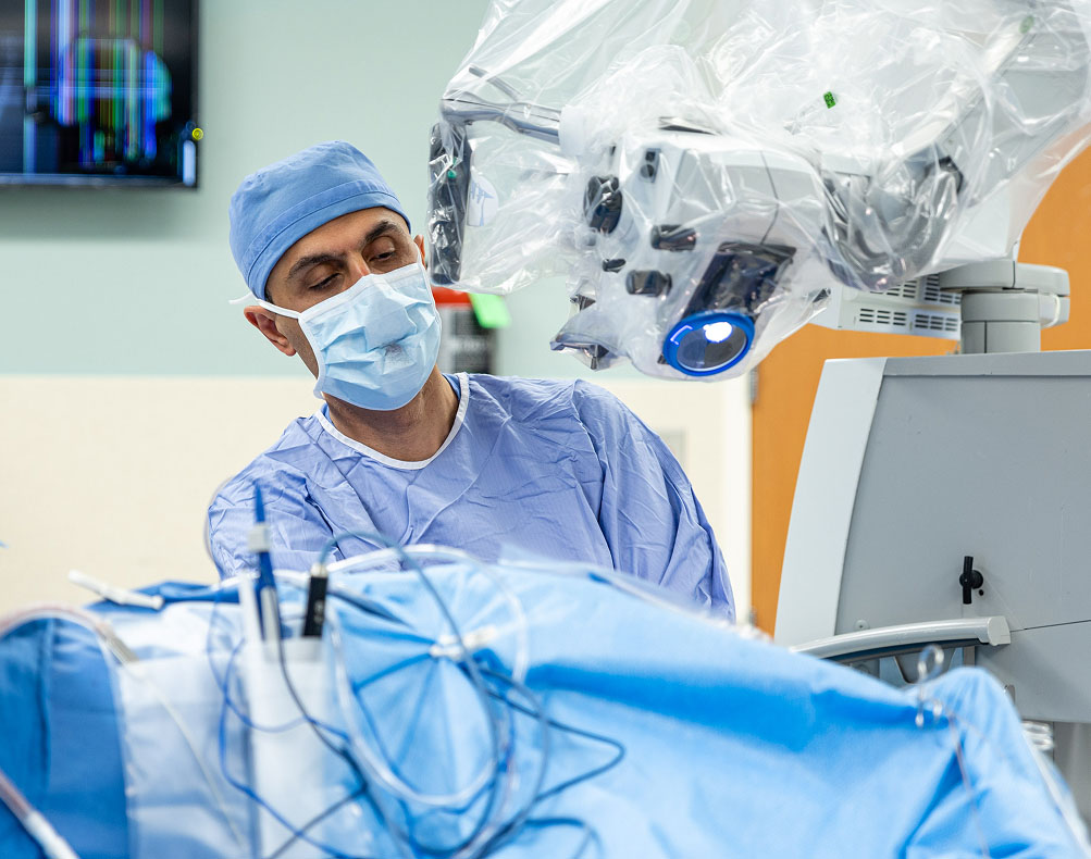 A surgeon in scrubs and a mask operates using advanced medical equipment in a sterile operating room.