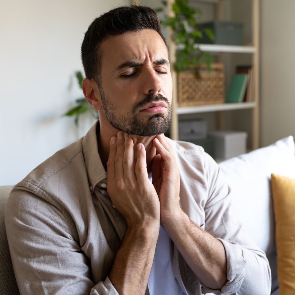 Man suffering from sore throat touching neck feeling pain. Copy space. Health and medical concepts.