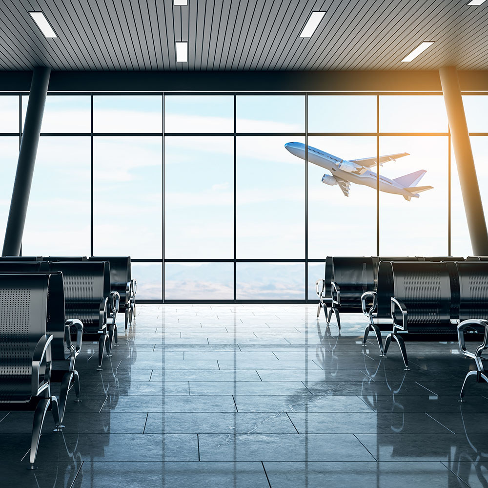 Modern airport waiting area with empty seats and a passenger airplane taking off outside the window at sunrise.